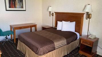 A hotel room with a large bed, two bedside tables, a desk, a chair, and a painting on the wall.