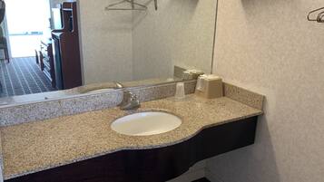 A bathroom with a granite countertop, a white sink, a mirror, and towel hooks.