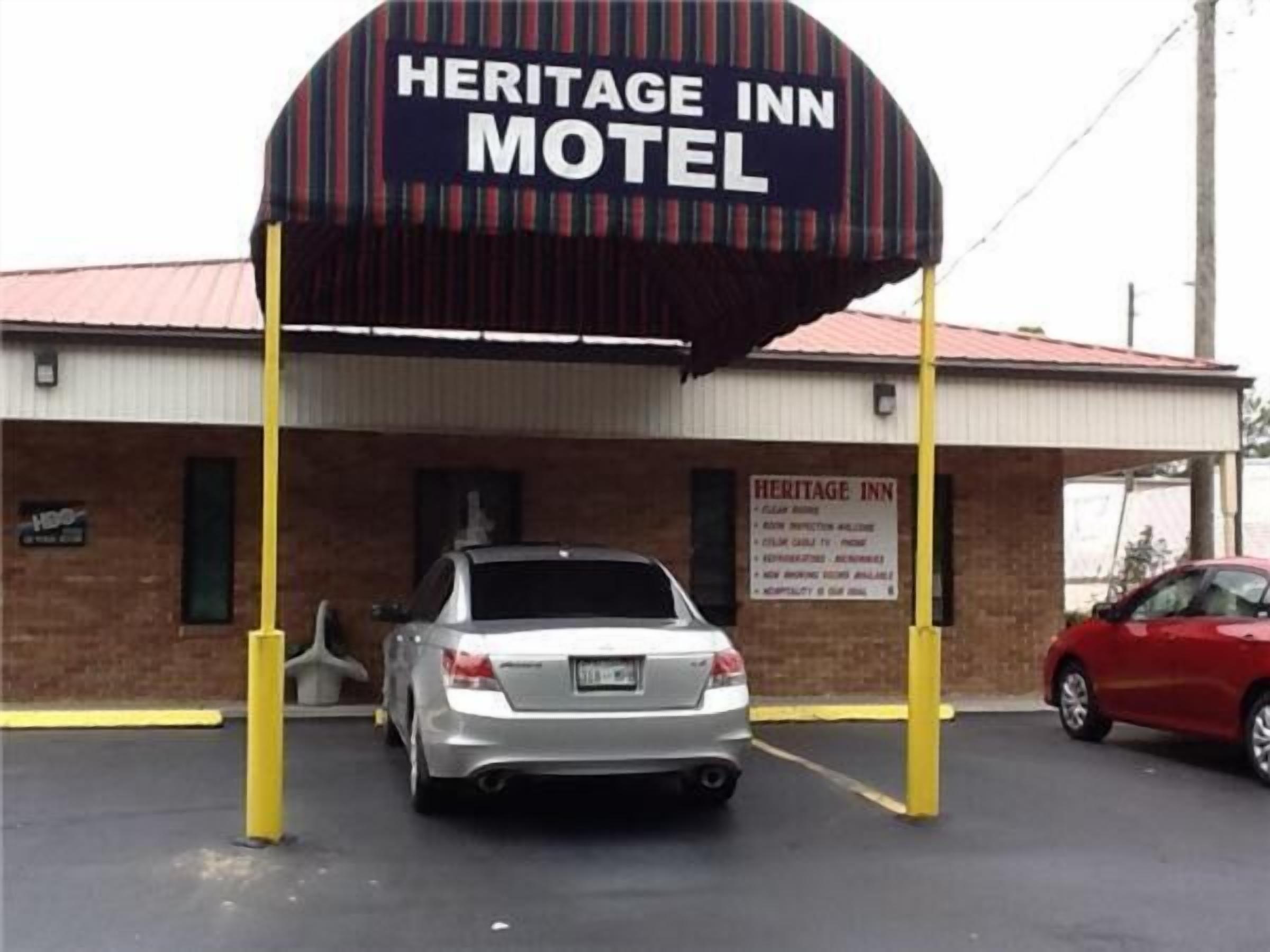 A Heritage Inn Motel with a prominent sign, a brick building, and a parking lot with two cars.