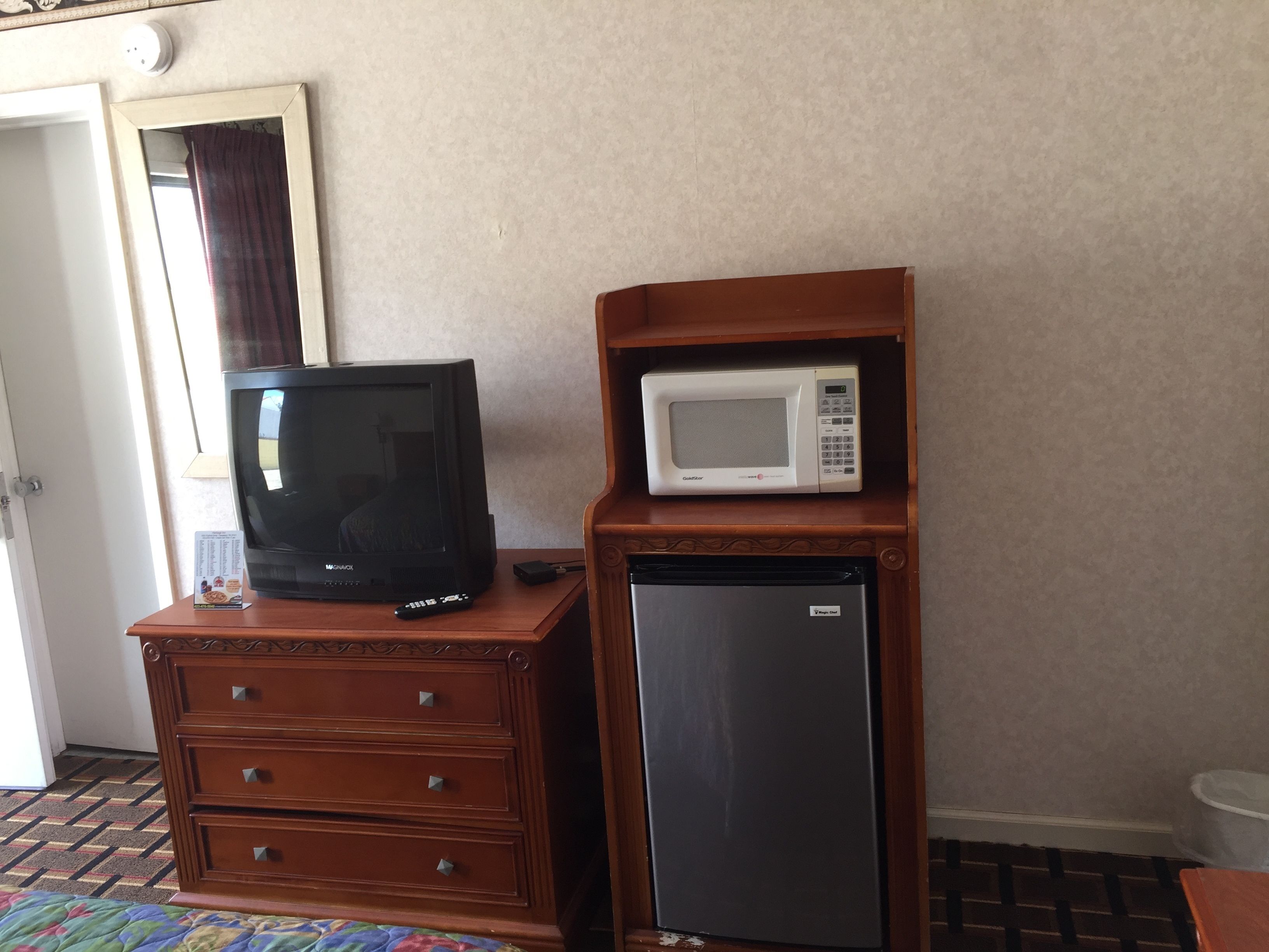 A wooden dresser with a television, a microwave, and a refrigerator.