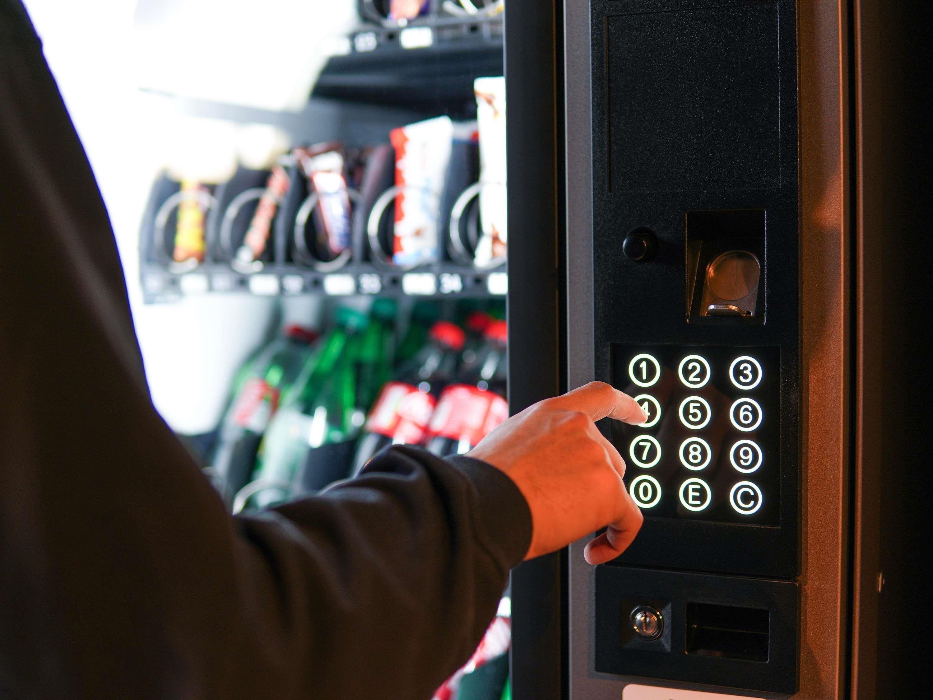A person using a keypad with illuminated numbers to interact with a machine, likely for a vending or self-service function.