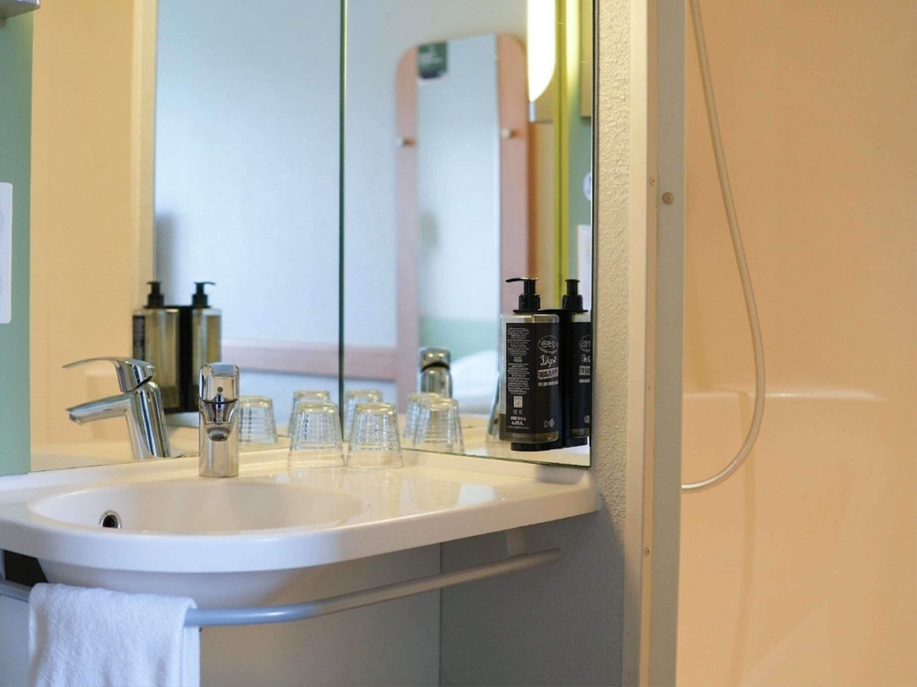 Un baño con un lavamanos blanco, un espejo y dos botellas negras sobre el mostrador.