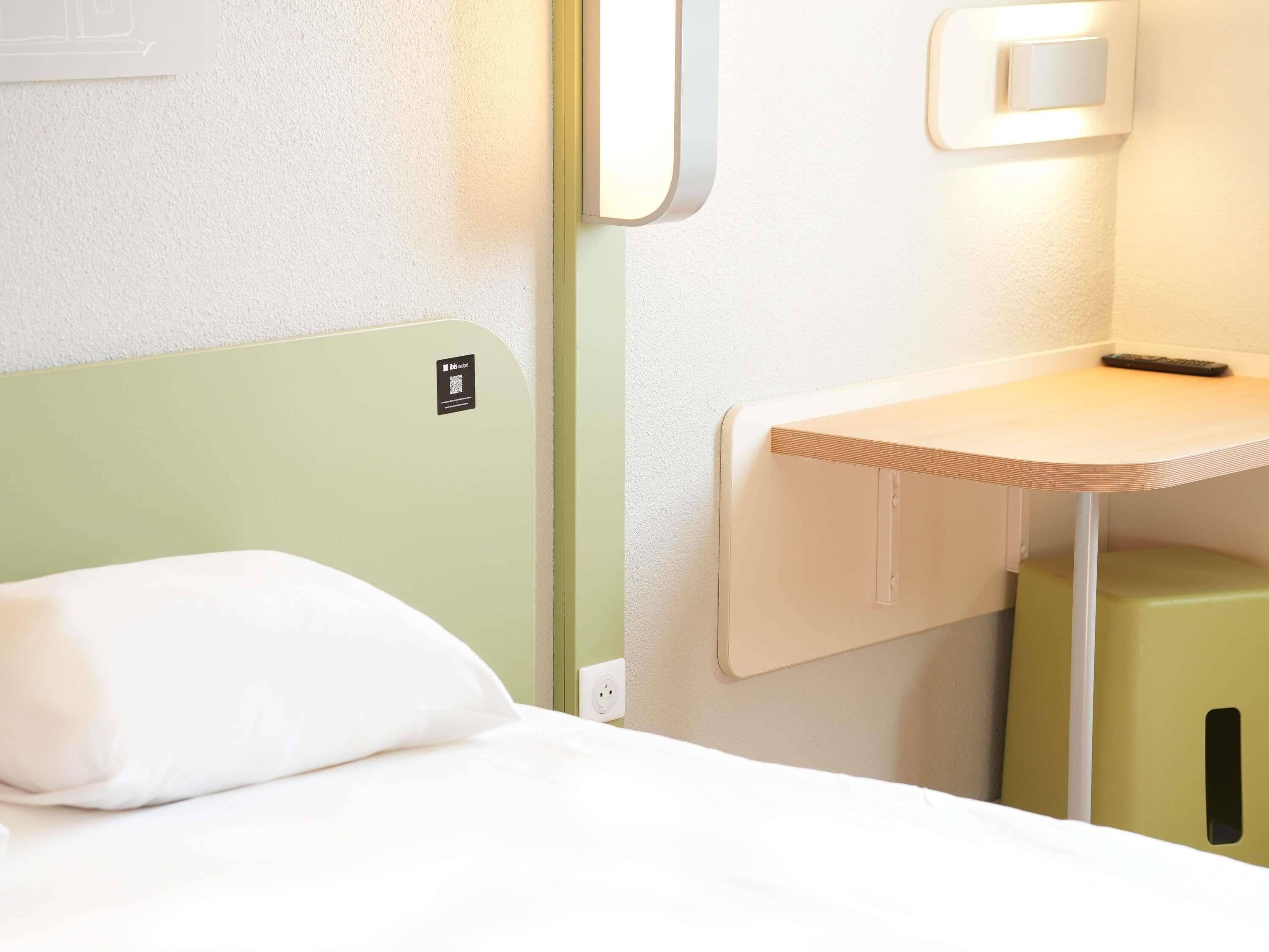 A bed with a green headboard, a bedside table with a remote control, and a green stool.