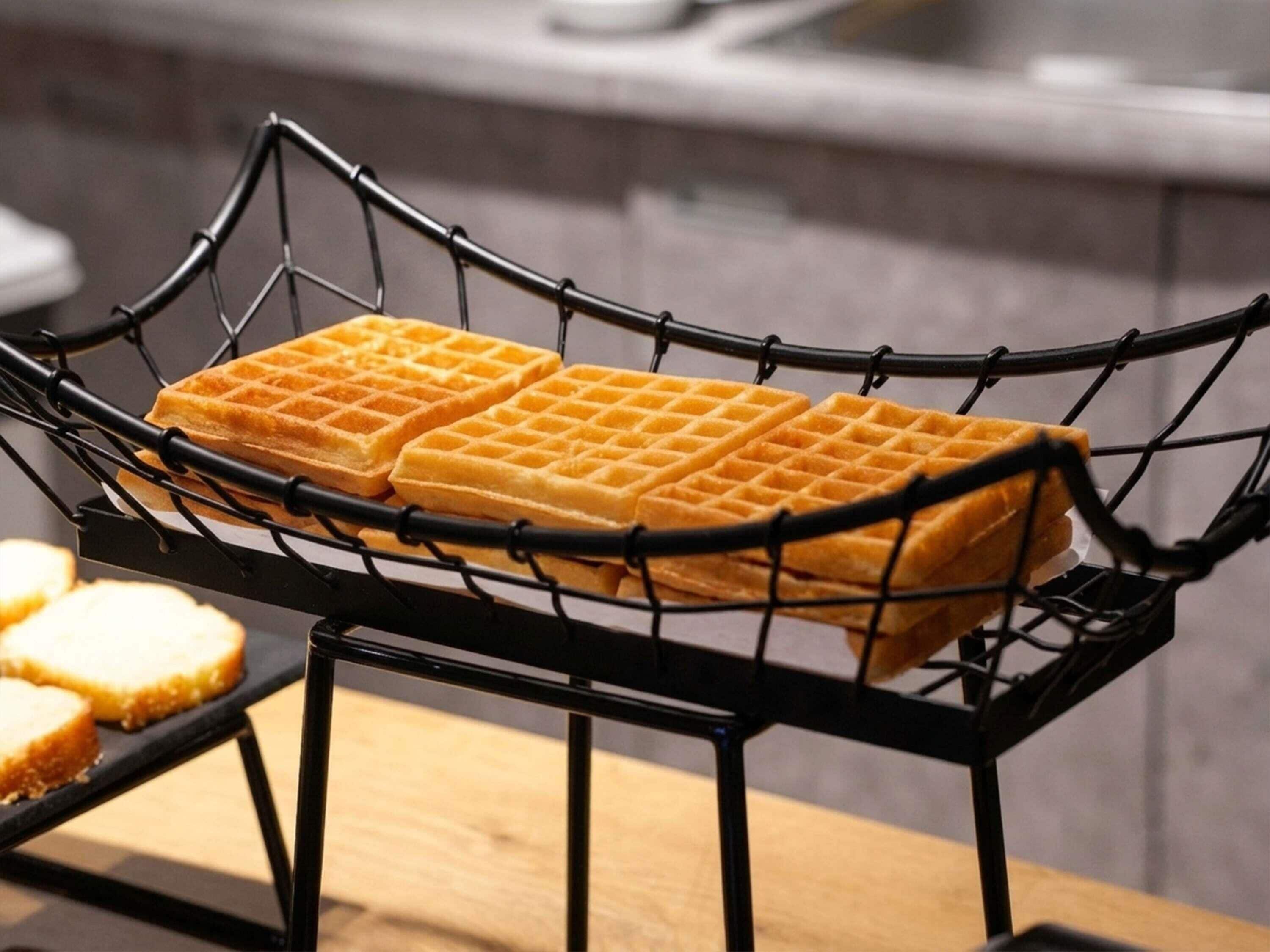 A waffle iron basket on a table with waffles inside.