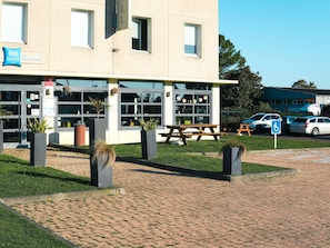 A building with large windows, a sign for ibis budget hotels, and a picnic table in the foreground. - ibis budget Caen Porte de Bretagne (Bretteville-sur-Odon)