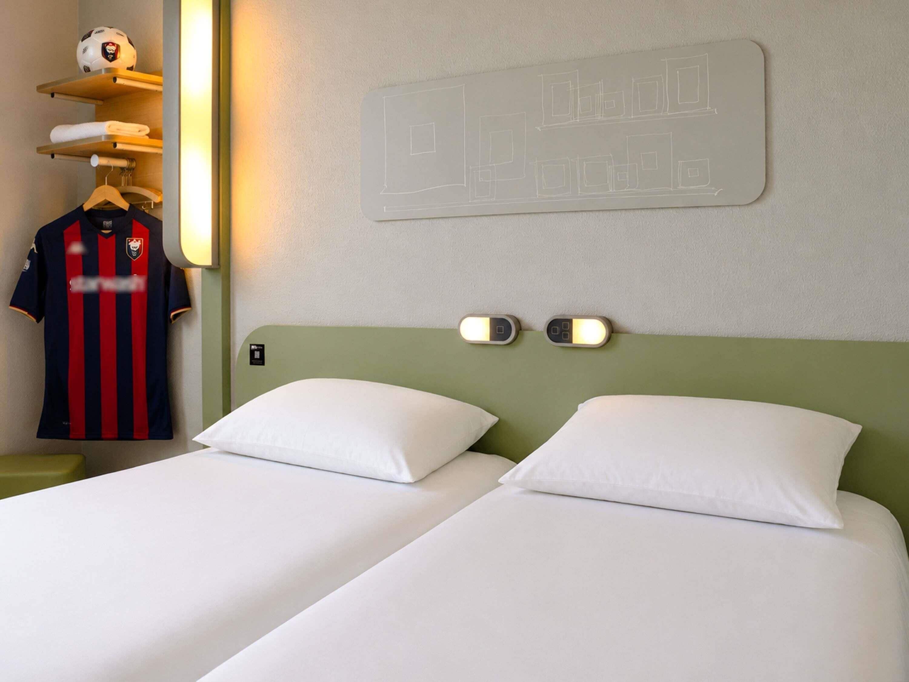 Habitación de hotel con dos camas, un reloj en la pared y una camiseta deportiva colgada.