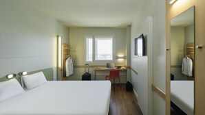 A hotel room with a bed, desk, chair, and a window with curtains.