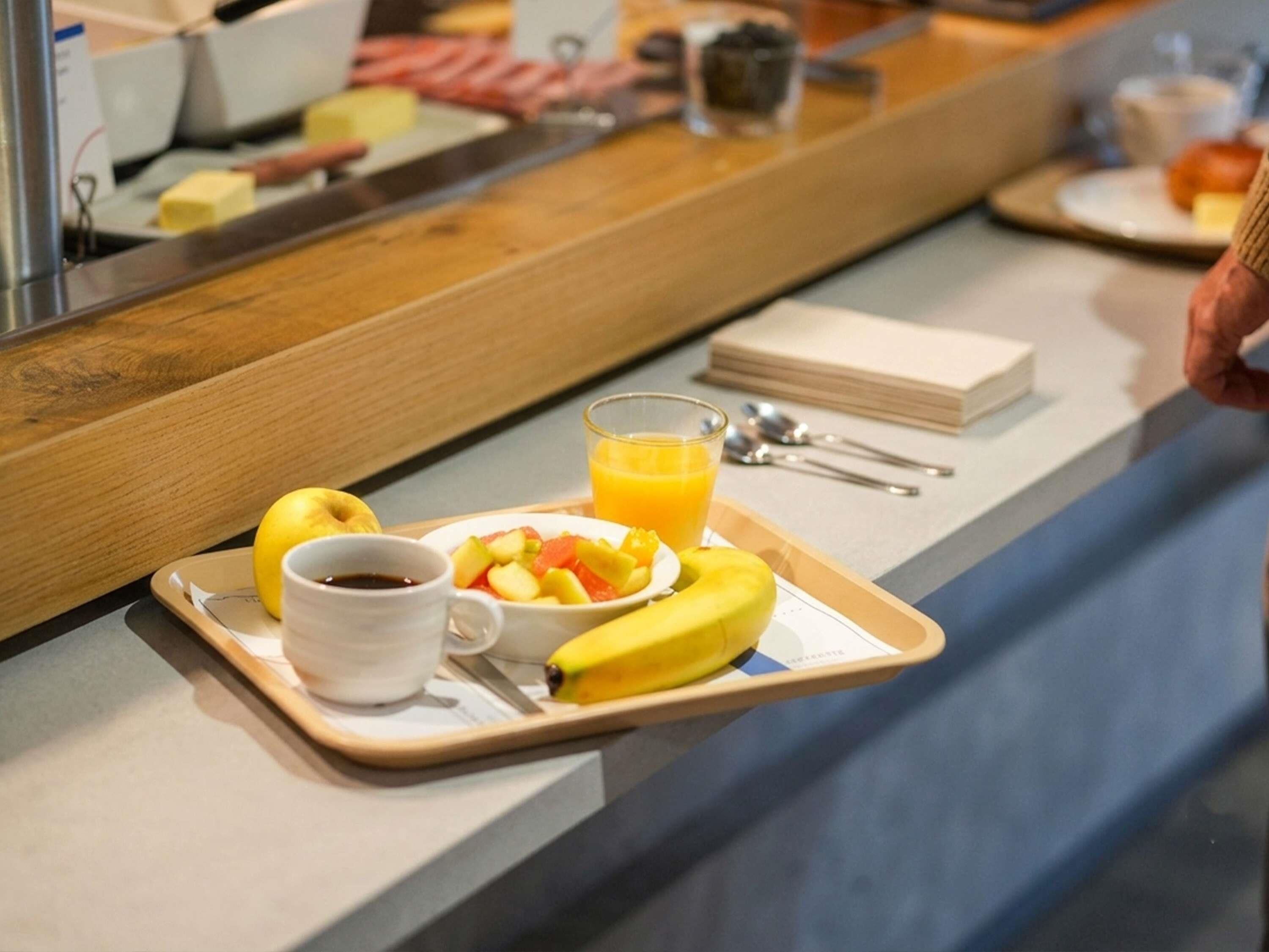 A breakfast tray with a banana, a glass of orange juice, and a cup of coffee on a wooden tray.