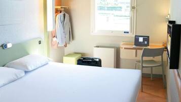 Une chambre d’hôtel avec un lit, un bureau avec un ordinateur portable, une chaise, un radiateur et une fenêtre.