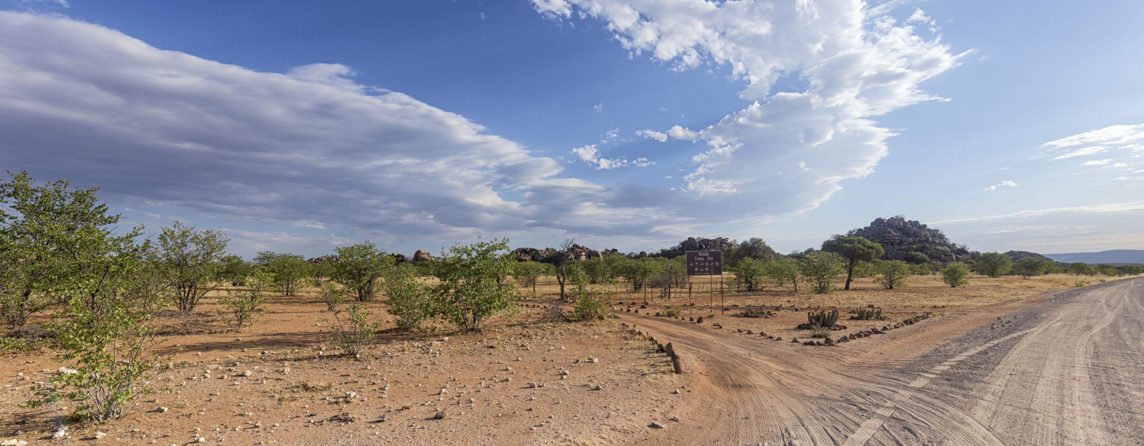 Paisatge de desert amb vegetació escassa, un camí de terra i un senyal que indica una zona de càmping.