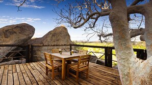 Une terrasse en bois avec une table et des chaises, offrant une vue sur un paysage pittoresque, avec de gros rochers et un ciel dégagé.