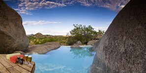 A pool surrounded by large rocks, with a view of the landscape and mountains in the background. - Hoada Camp Site (Palmwag)