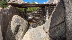 Une construction rustique servant de toilettes extérieures, intégrée à un paysage rocheux et dotée d’un toit en bois.
