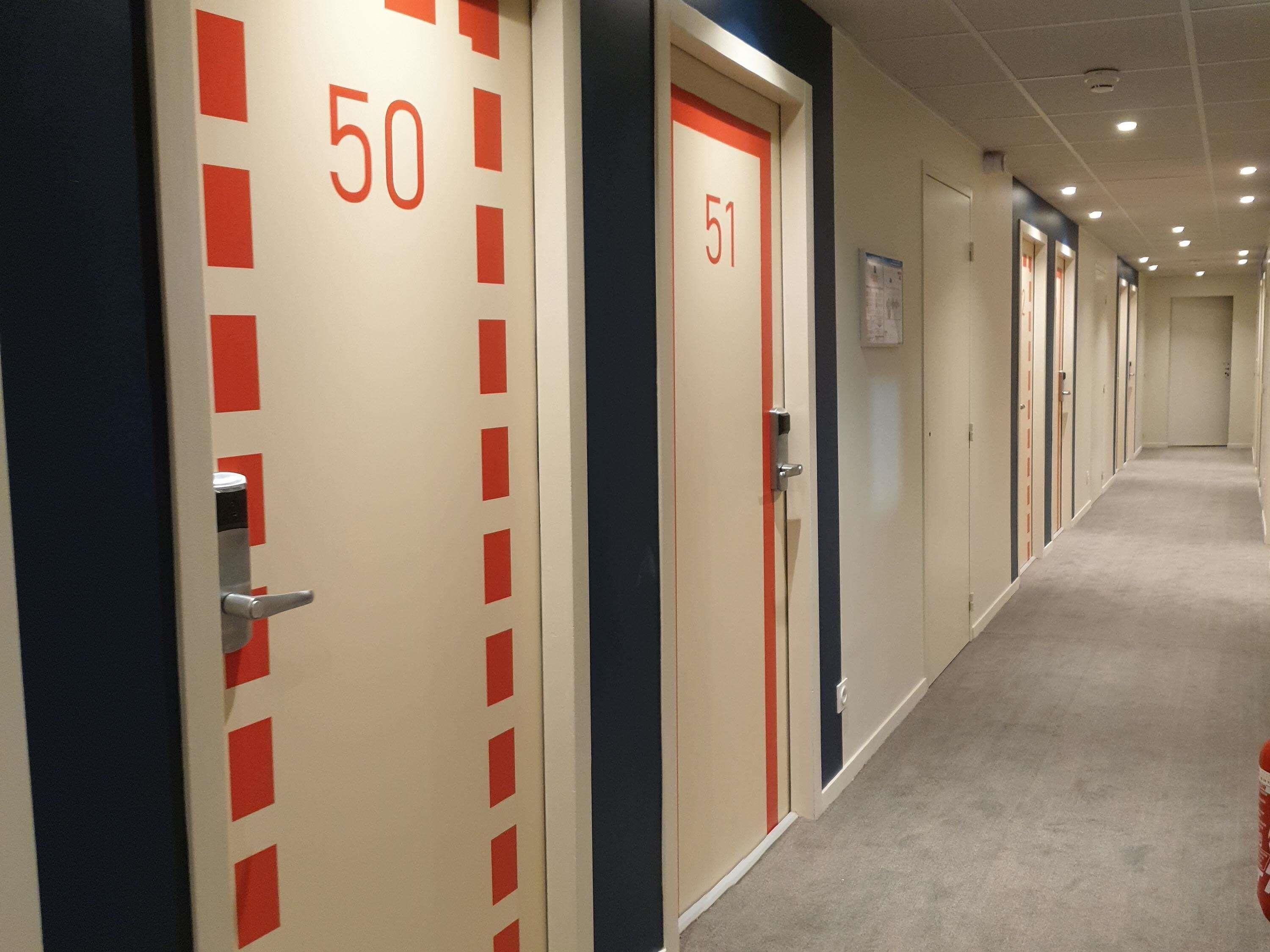 A hotel corridor with doors numbered 50 and 51, carpeted floors, and a ceiling with recessed lighting.