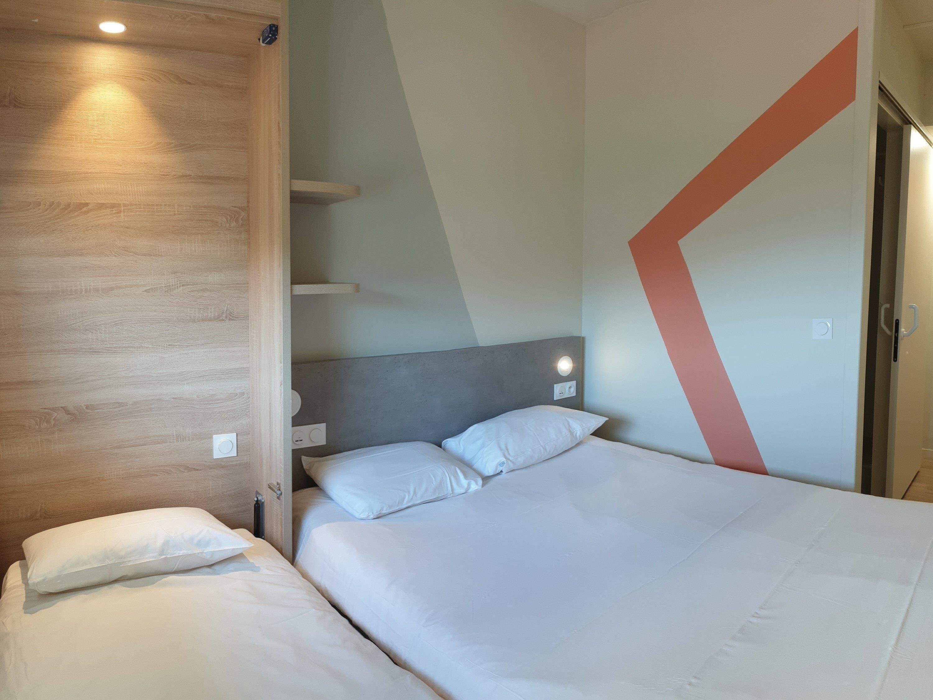 Ein modernes Hotelzimmer mit einem großen Bett, einem Holz-Kopfteil und einem geometrischen Wanddesign.