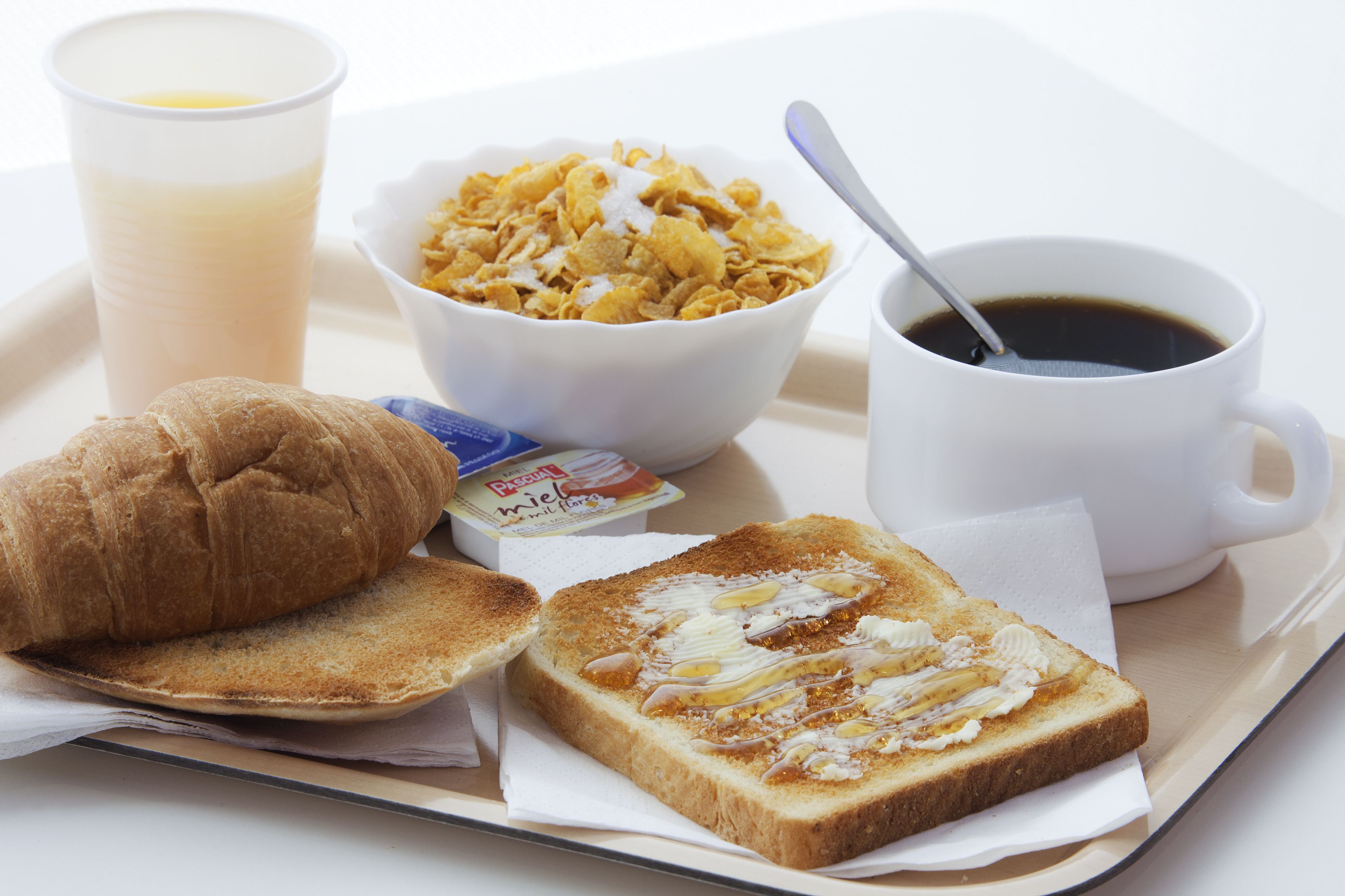 A tray with a croissant, two slices of toast with butter and jam, a bowl of cereal, a cup of coffee, and a carton of milk.