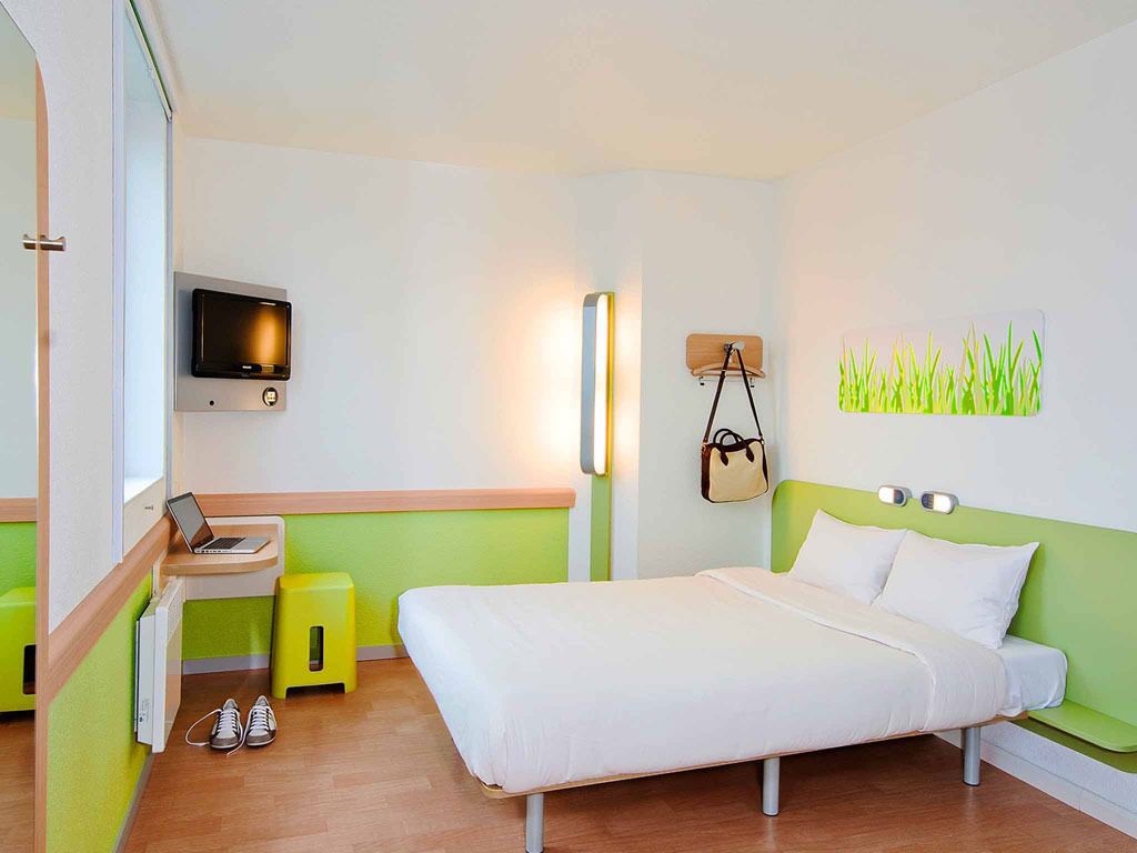 Una habitación de hotel moderna con cama, escritorio, silla, televisor y un perchero en la pared.