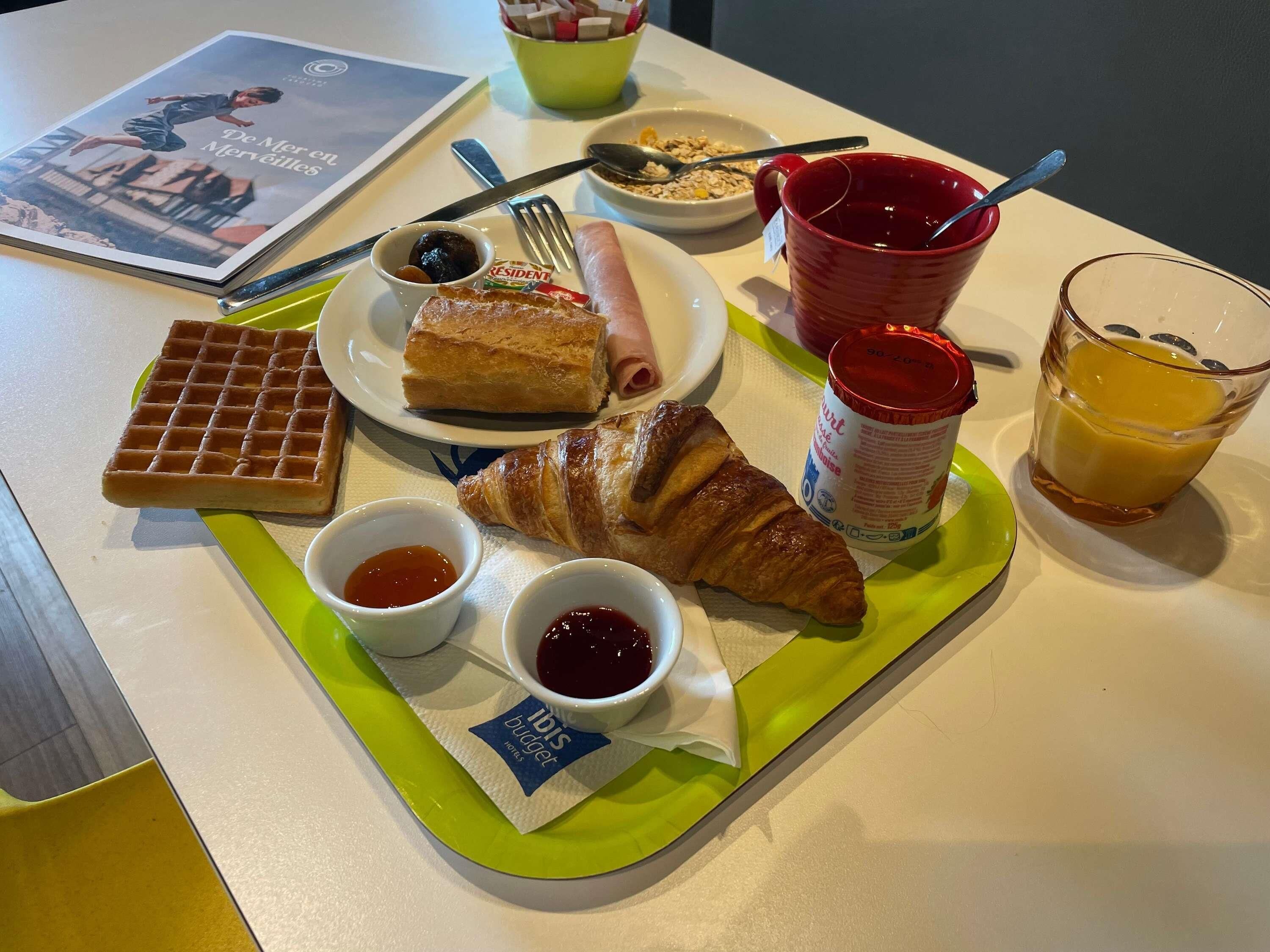 Un plateau de petit-déjeuner avec des gaufres, des croissants, de la confiture et une boisson.