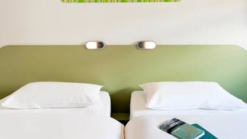 Une chambre d’hôtel avec deux lits, du linge de lit blanc, une tête de lit verte et un luminaire fixé au mur.