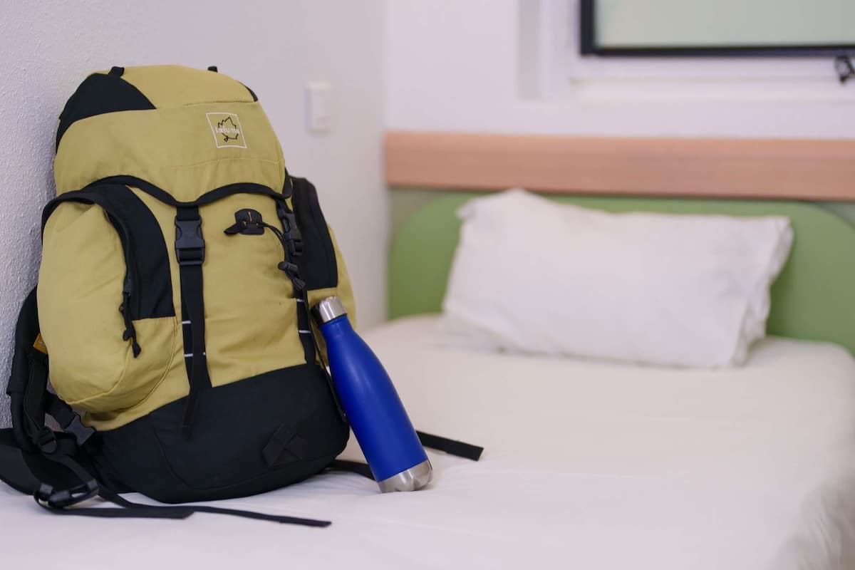 A bed with a white pillow and a yellow backpack with a blue water bottle on it.
