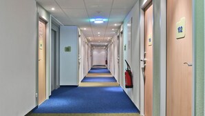 Pasillo de hotel con puertas numeradas 102 y 103, alfombra azul y señalización de salida de emergencia.
