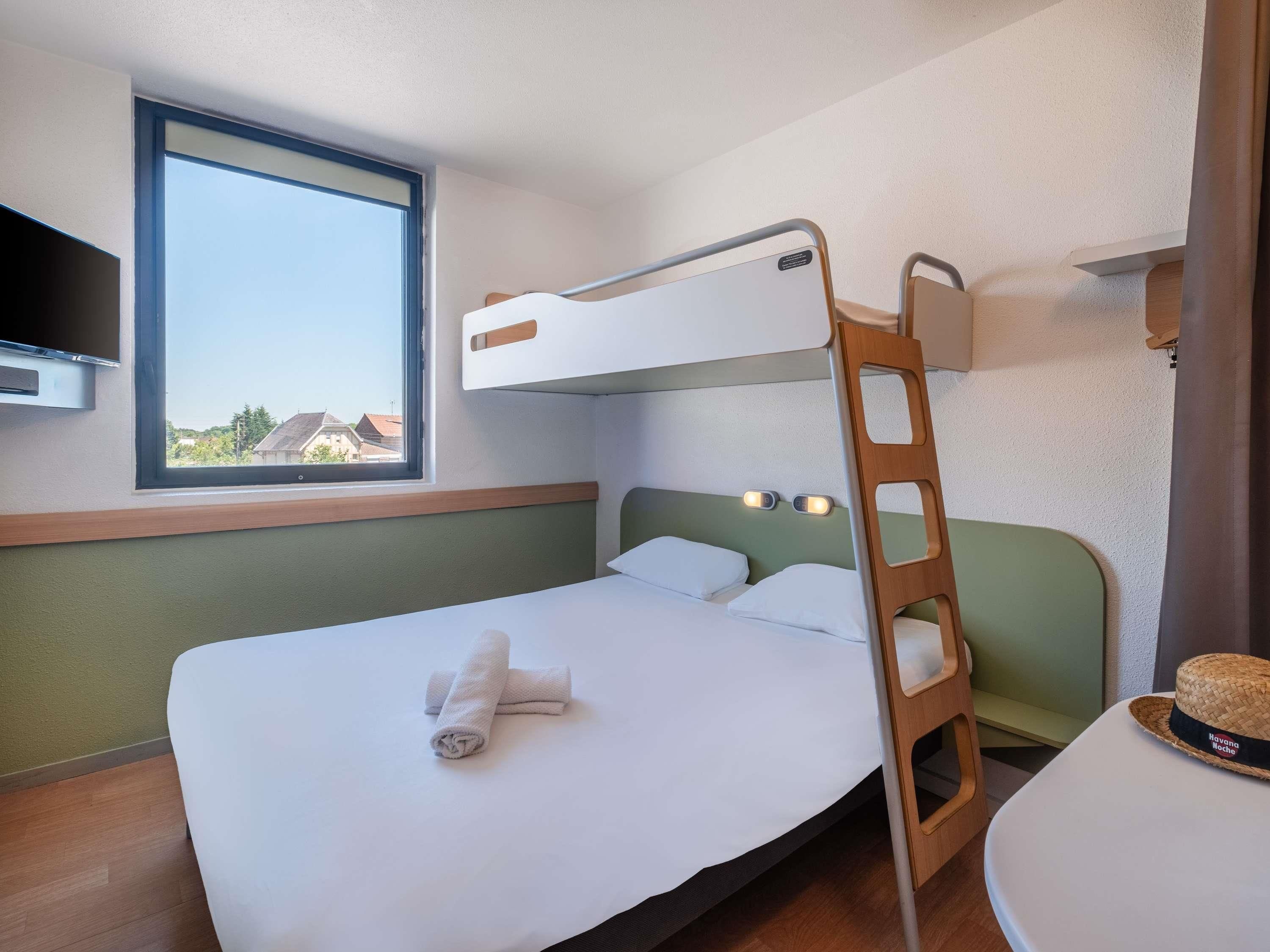 A bunk bed with a ladder, a bedside table, a window with a view, and a wall-mounted light fixture.