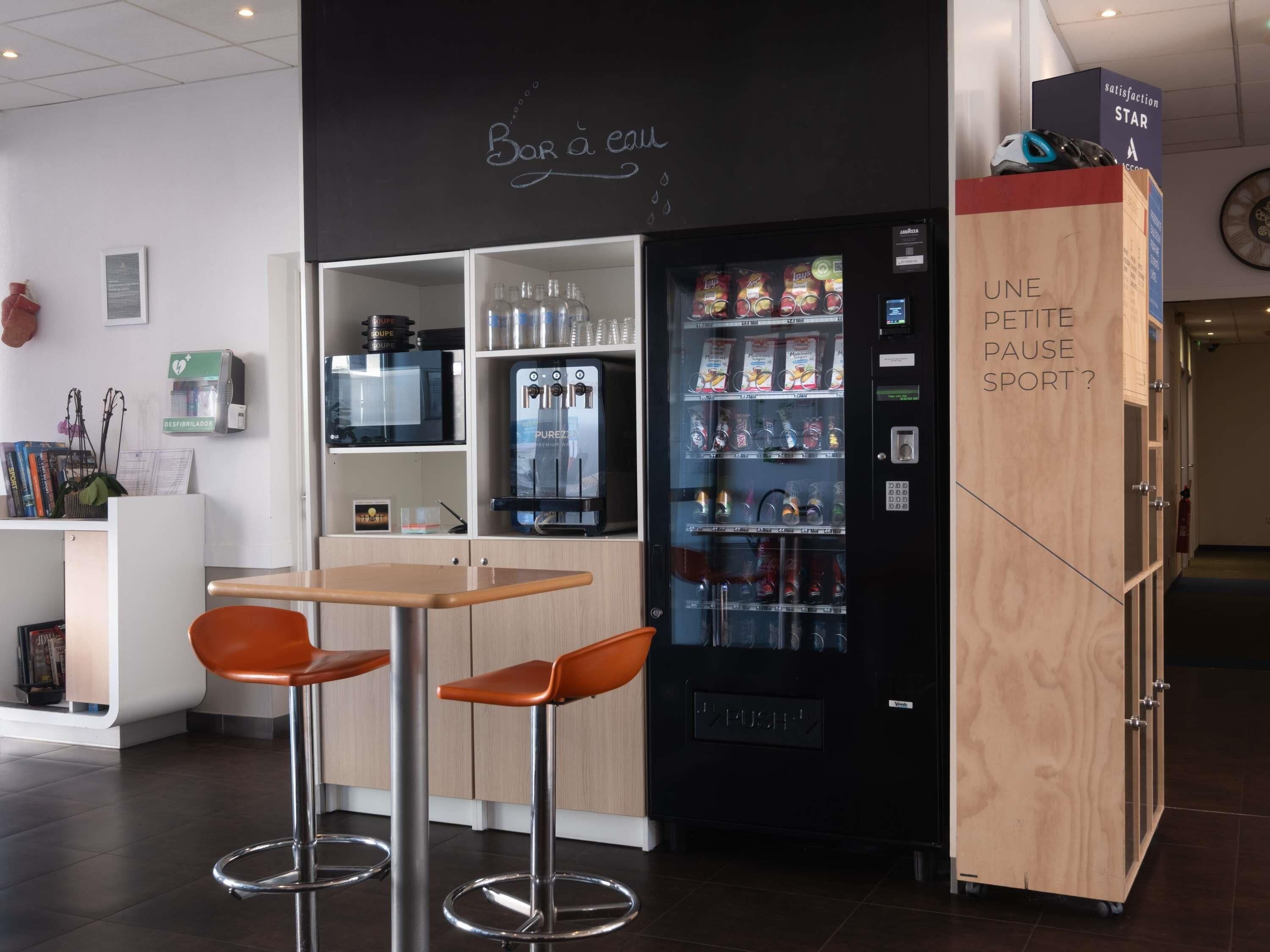 Un espace bar moderne équipé d’un distributeur automatique, de deux tabourets et d’un purificateur d’air fixé au mur.