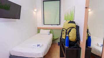 A small hotel room with a single bed, a desk, a chair, a window with a view, a flat-screen TV, and a wall-mounted artwork.