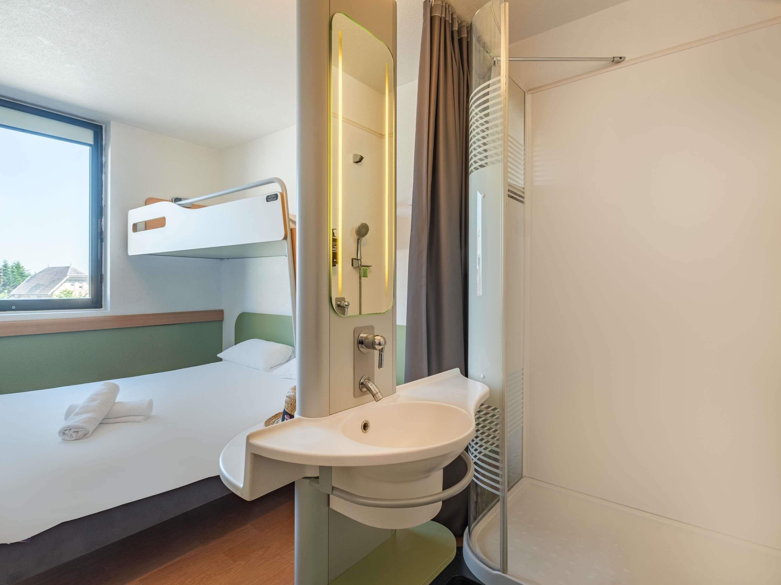 A hotel room with a bunk bed, a bathroom with a sink and mirror, and a shower.