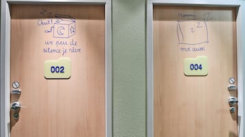 Two hotel room doors with numbers 002 and 004. Each door has a small sign with a noise level indicator and a hand-drawn icon representing a sleeping person.