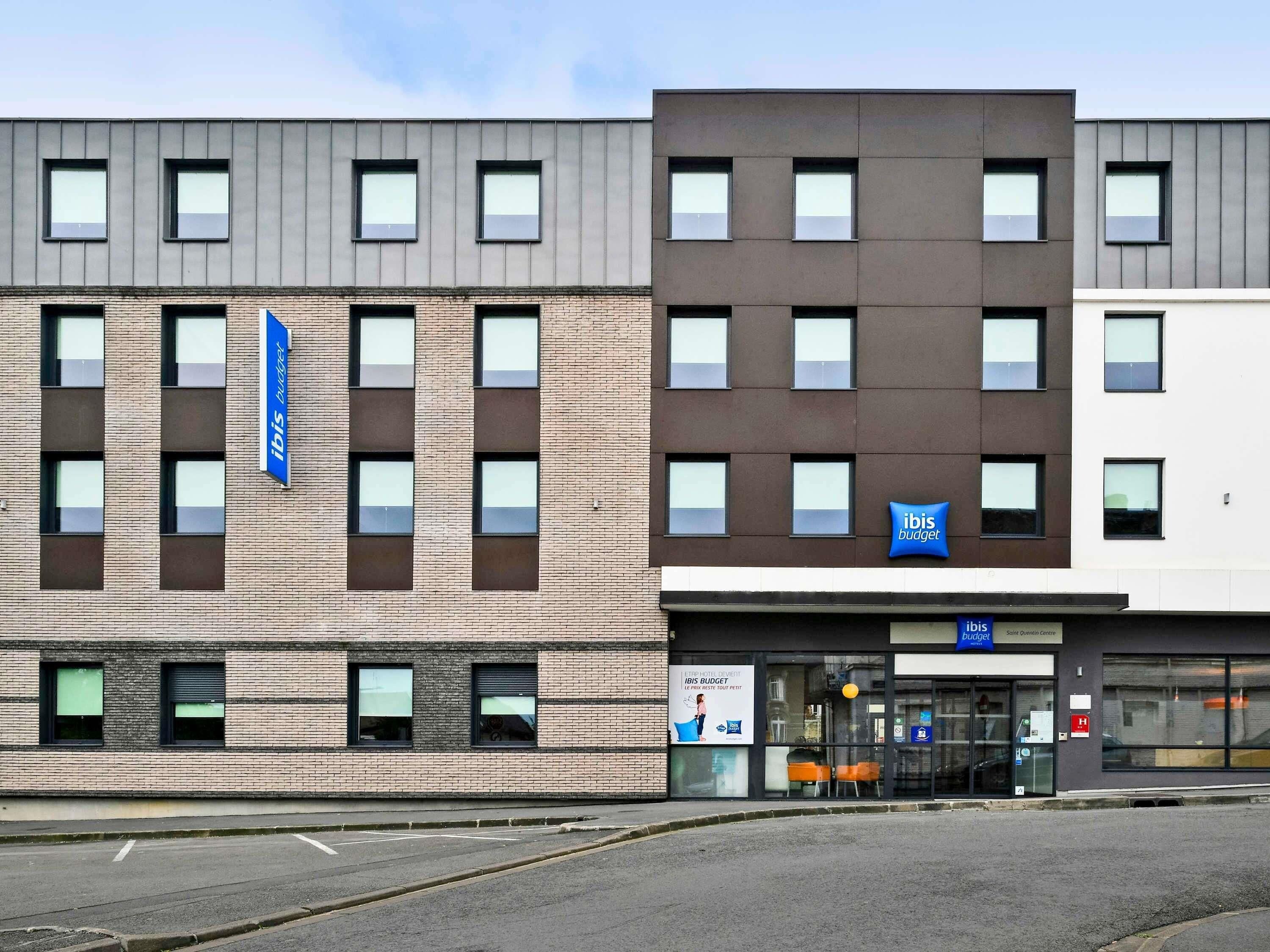 A modern hotel building with multiple windows and a sign for 'Ibis Budget.'