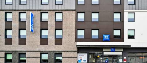 A modern hotel building with multiple windows and a sign for 'Ibis Budget.'