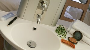 Un baño con un lavamanos blanco, un espejo y un televisor montado en la pared.