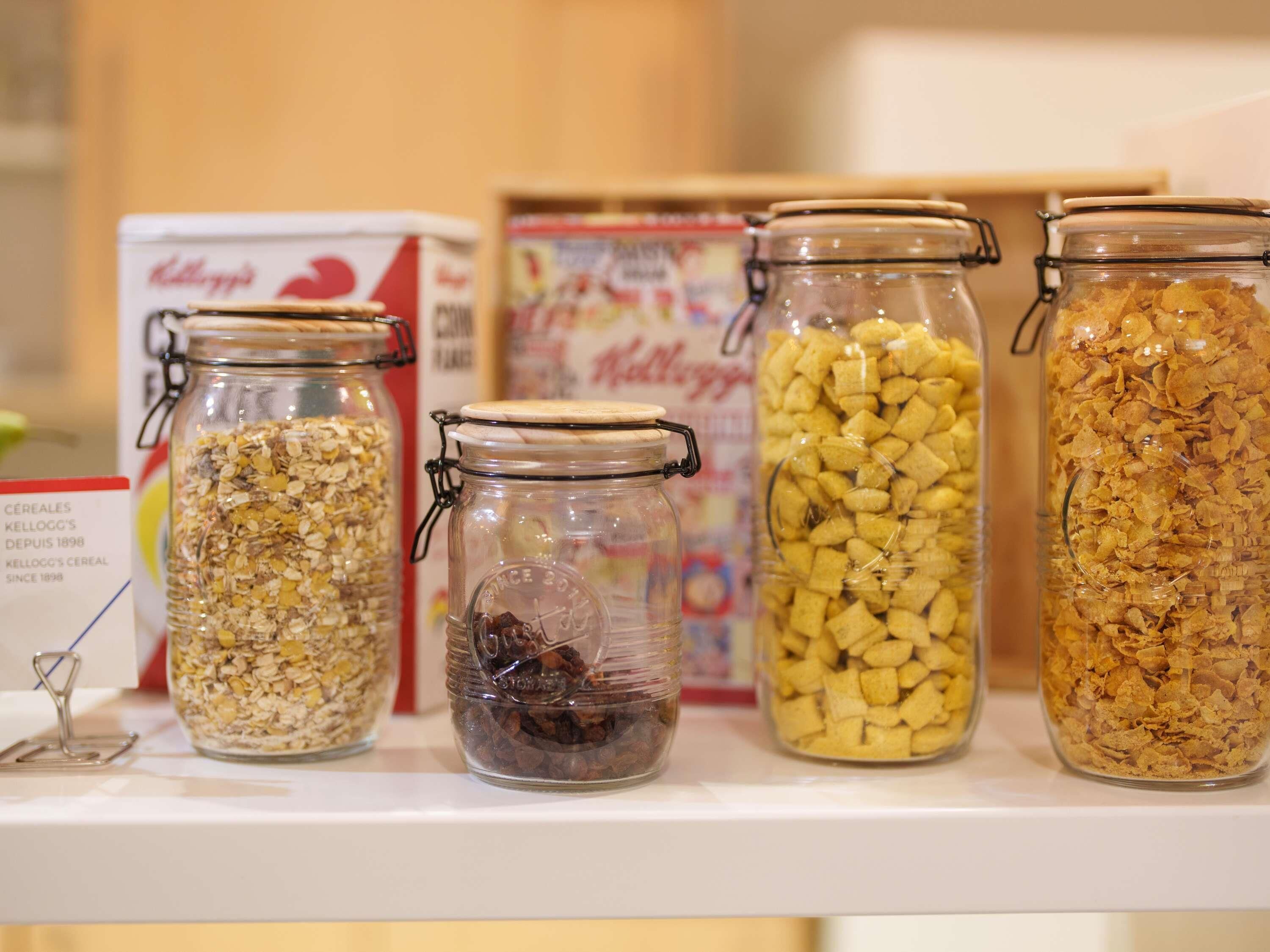 Four glass jars with different contents on a shelf, with cereal boxes in the background.