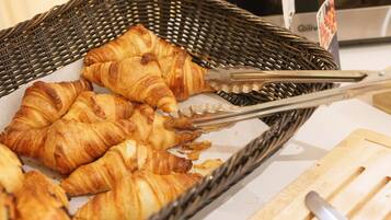 A basket of croissants on a table with a knife and tongs nearby.