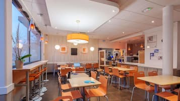 A modern restaurant interior with multiple dining tables and chairs, a bar area, and a seating section with a view of the outdoors.