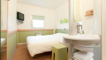 A hotel room with a bed, a bedside table, a TV, a window, a sink, and a mirror.