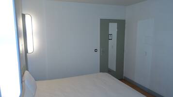 A simple, unadorned room with a bed, a door, and a light switch on the wall.
