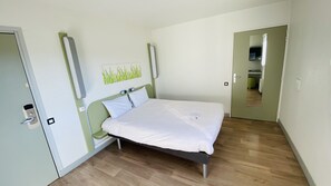 Quarto com cama, porta, espelho e luminária fixada na parede.