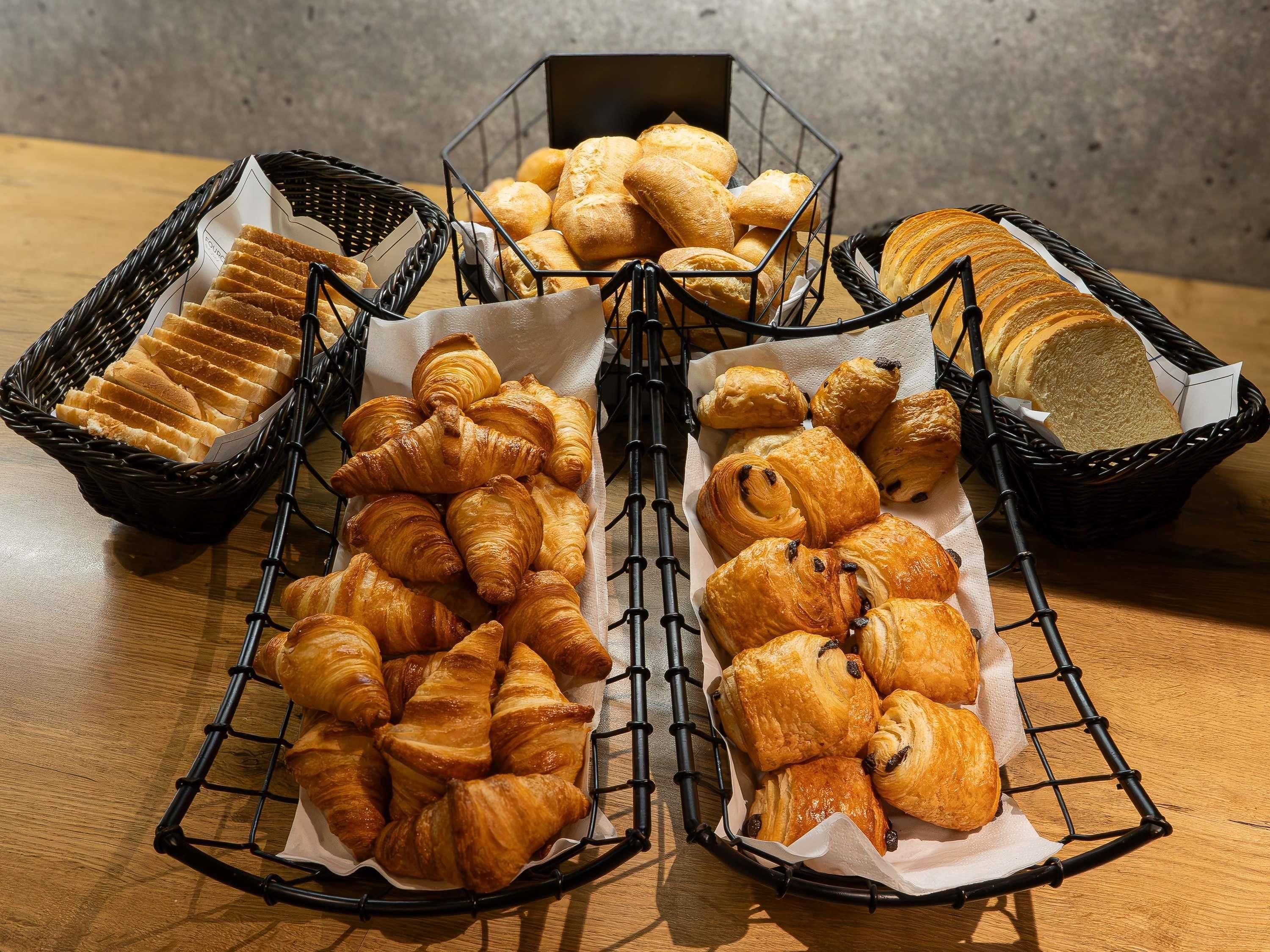 A variety of baked goods including bread and croissants arranged in baskets on a wooden table.