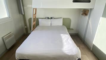A bunk bed room with a white mattress, a wooden floor, and a window on the left.