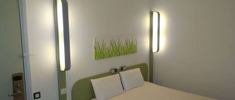 A single bed with a green headboard, white bedding, and two wall-mounted light fixtures.
