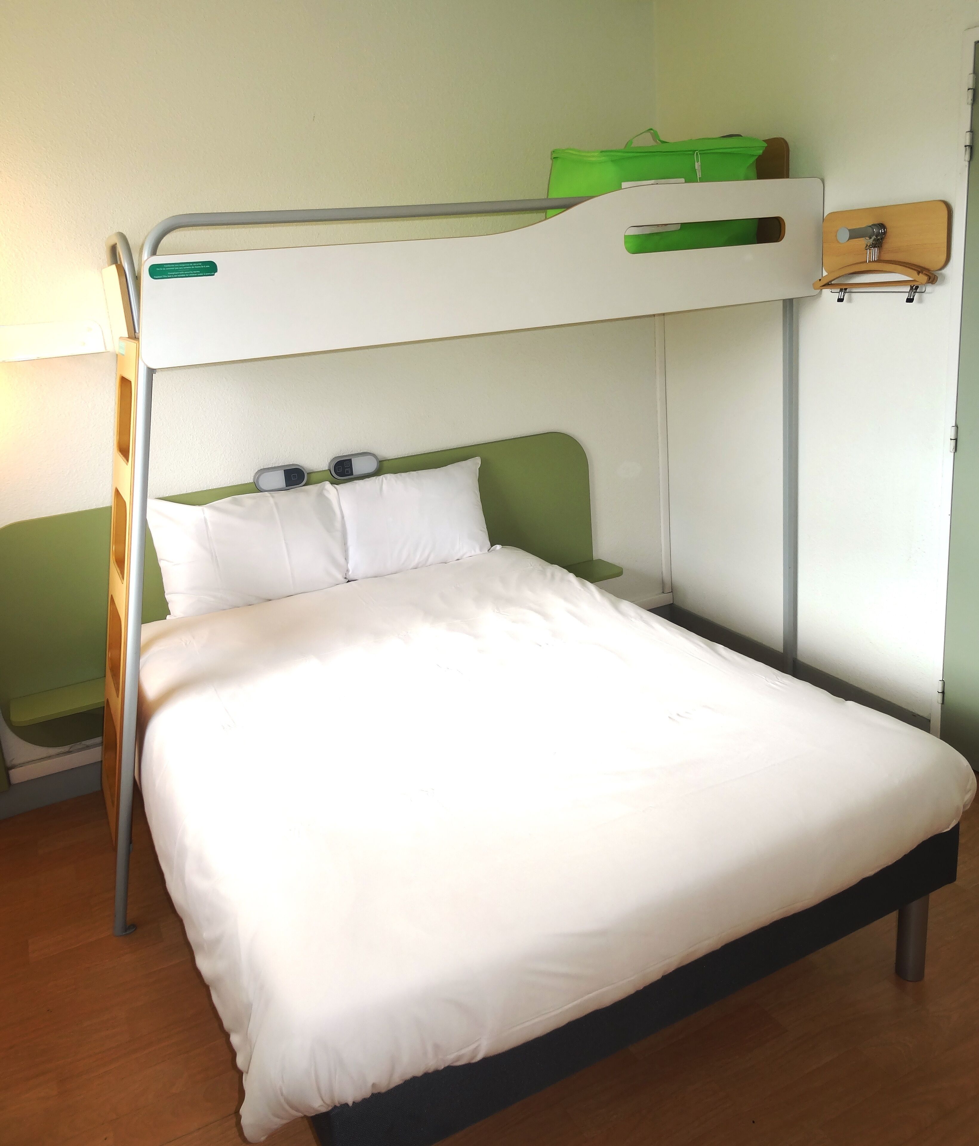 A bunk bed with a green headboard, white bedding, and a small green bag on the top bunk.