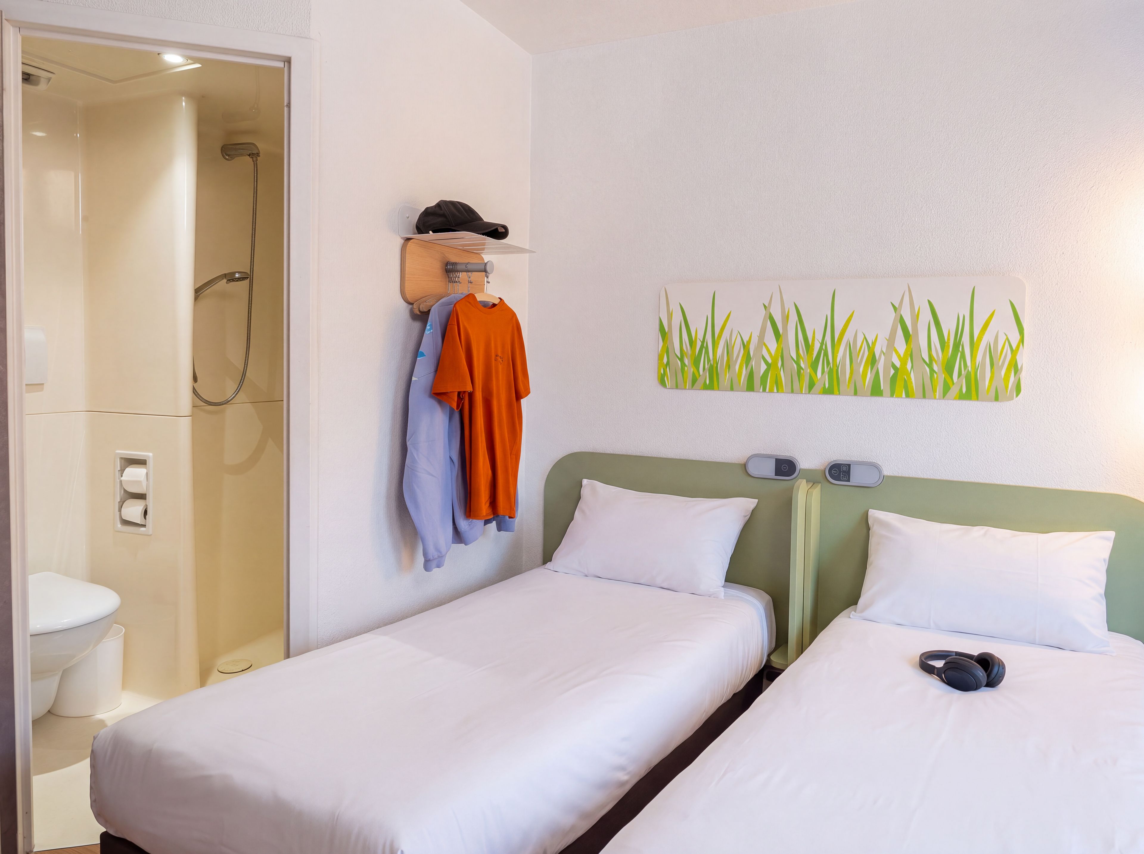 Habitación de hotel con dos camas, ducha, un perchero con ropa y una obra de arte en la pared.