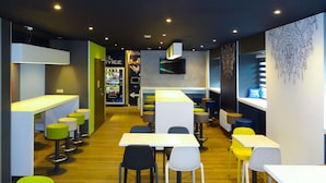 A modern restaurant with a bar area, seating with stools and tables, and a vending machine in the background. - ibis budget Caen Centre Gare (Caen)