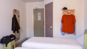 A hotel room with two beds, a mirror, a door, and a coat rack with a jacket and a shirt.