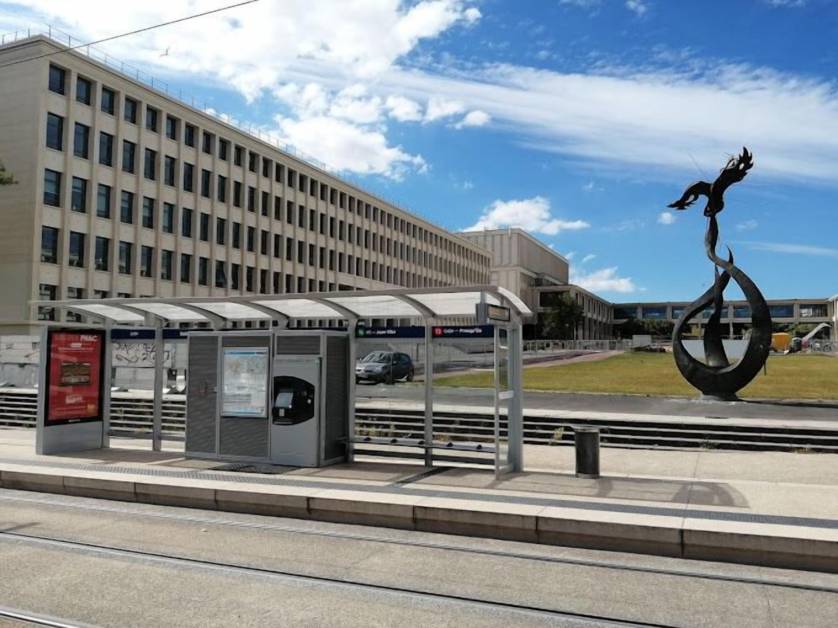A bus stop with a shelter, a trash bin, and a sculpture.