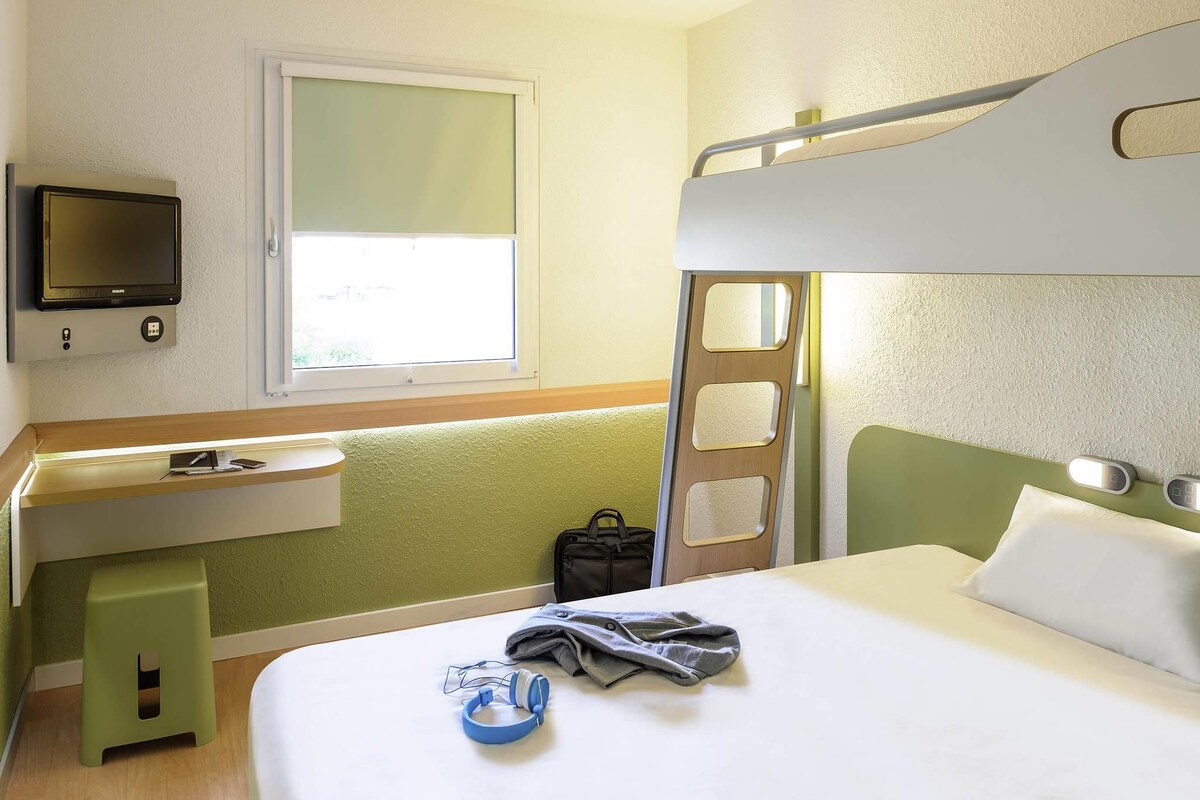 Hotellihuone, jossa on kerrossänky, työpöytä tuolilla, televisio ja ikkuna.