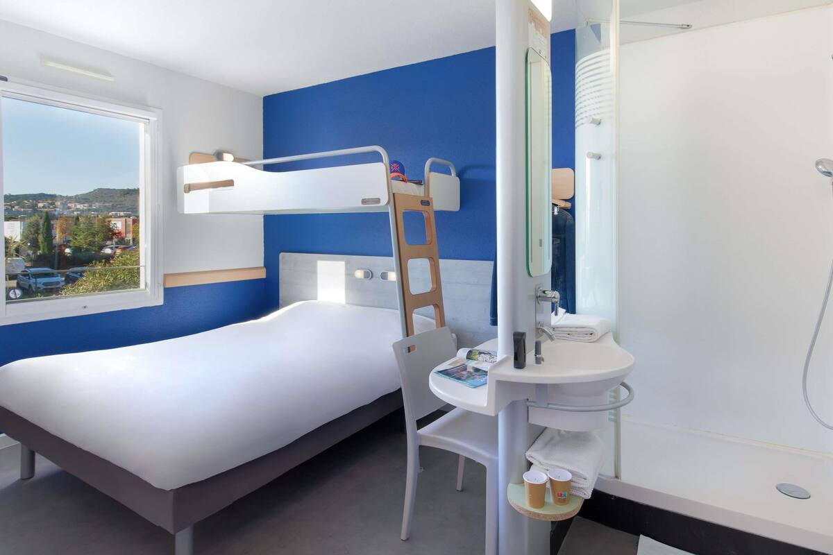 A bunk bed with a ladder, a desk, and a bathroom with a shower.
