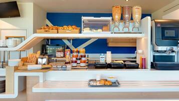 A breakfast bar with pastries, condiments, and a coffee machine.